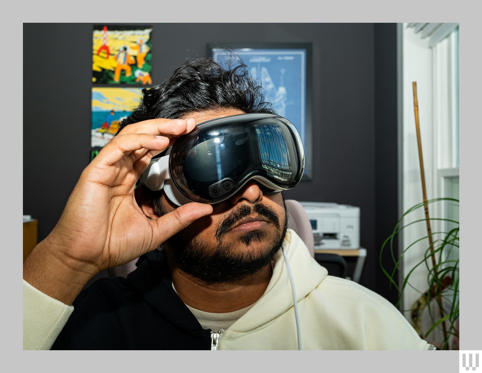 Person sitting in home office wearing sleek black and silver virtual reality headset one hand gripping the side