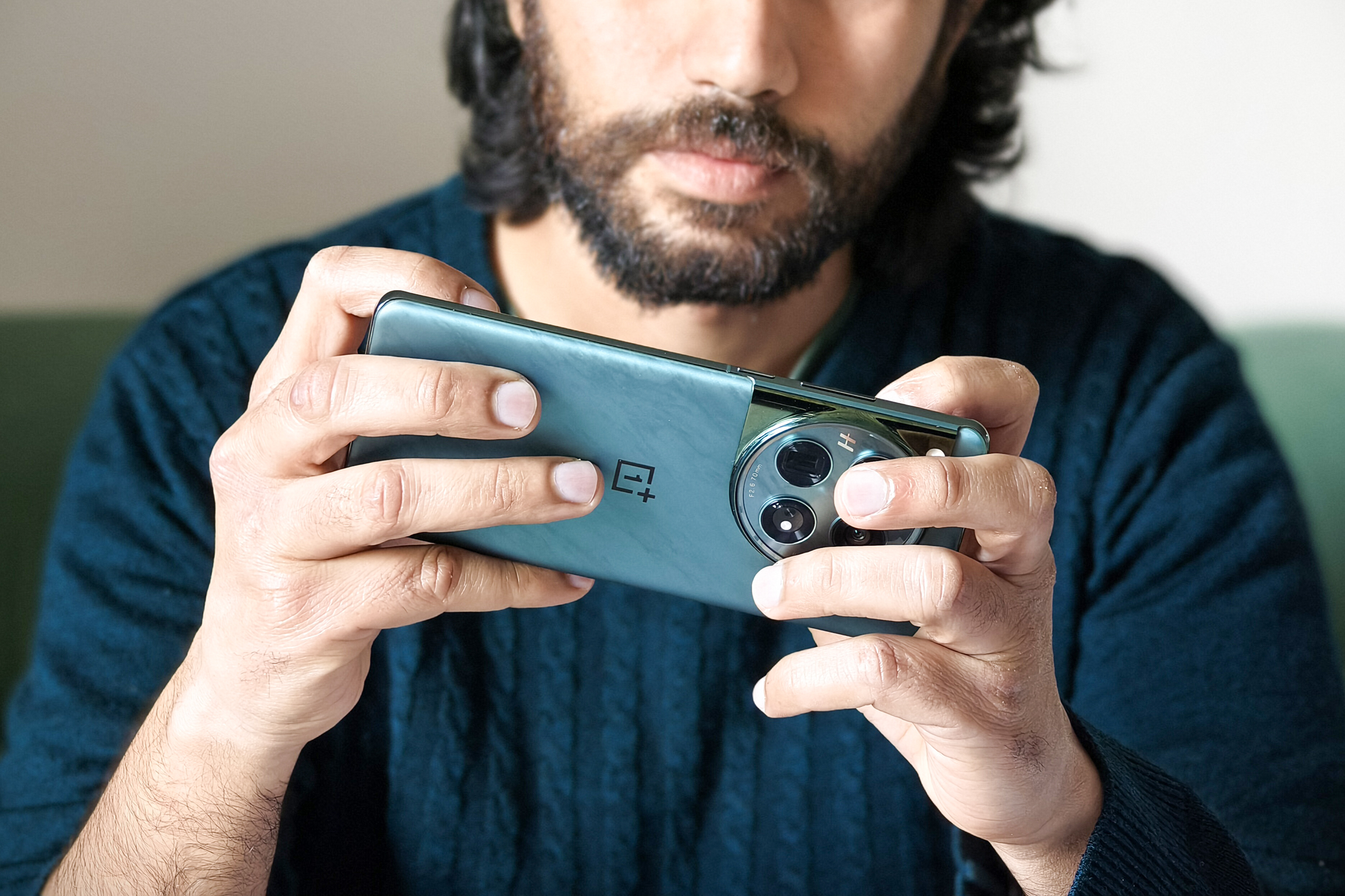 Person holding​ green OnePlus 12 phone in hands while playing games.