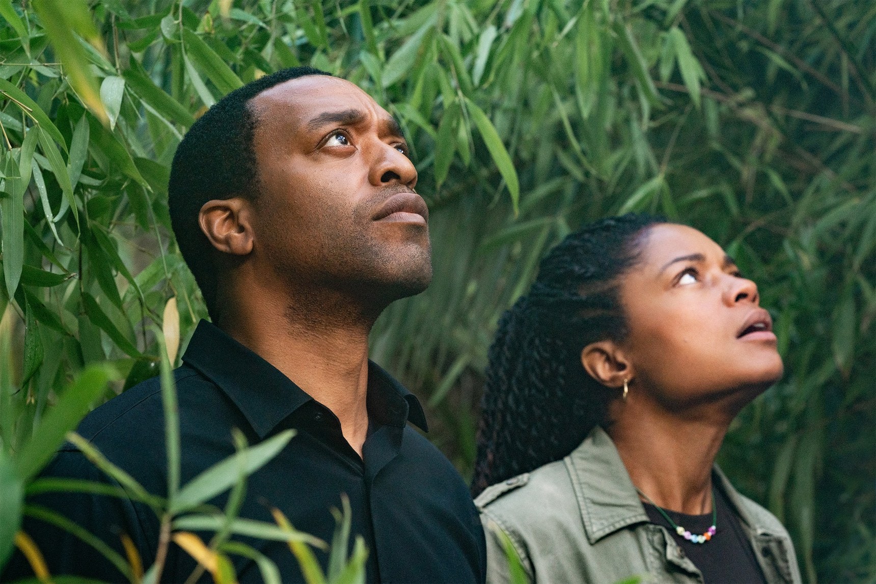 Chiwetel Ejiofor and⁢ Naomie‍ Harris ​(Justin⁣ Falls) looking up while surrounded by green trees