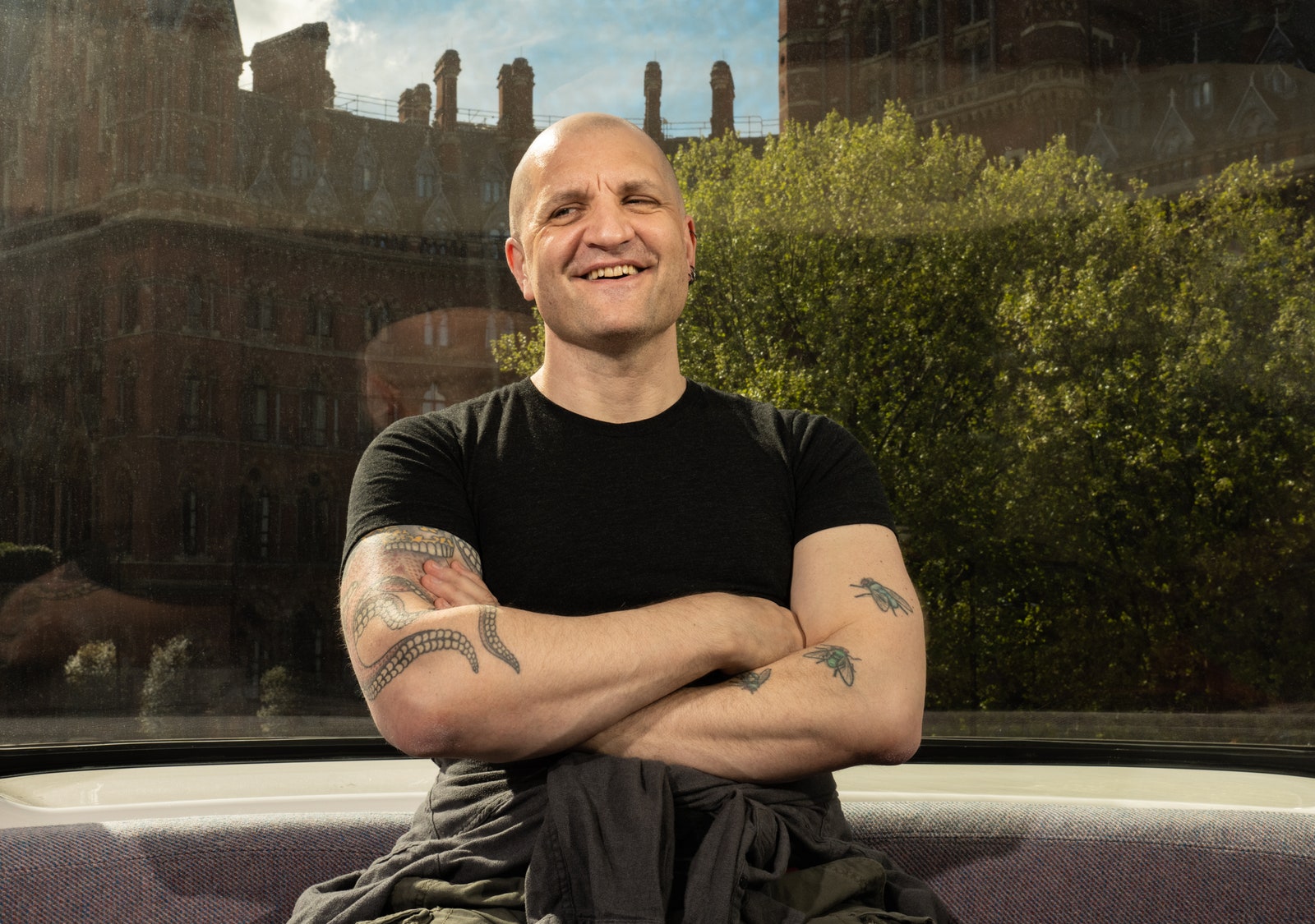 China Miville smiling while sitting in front of a window with a view of London behind him